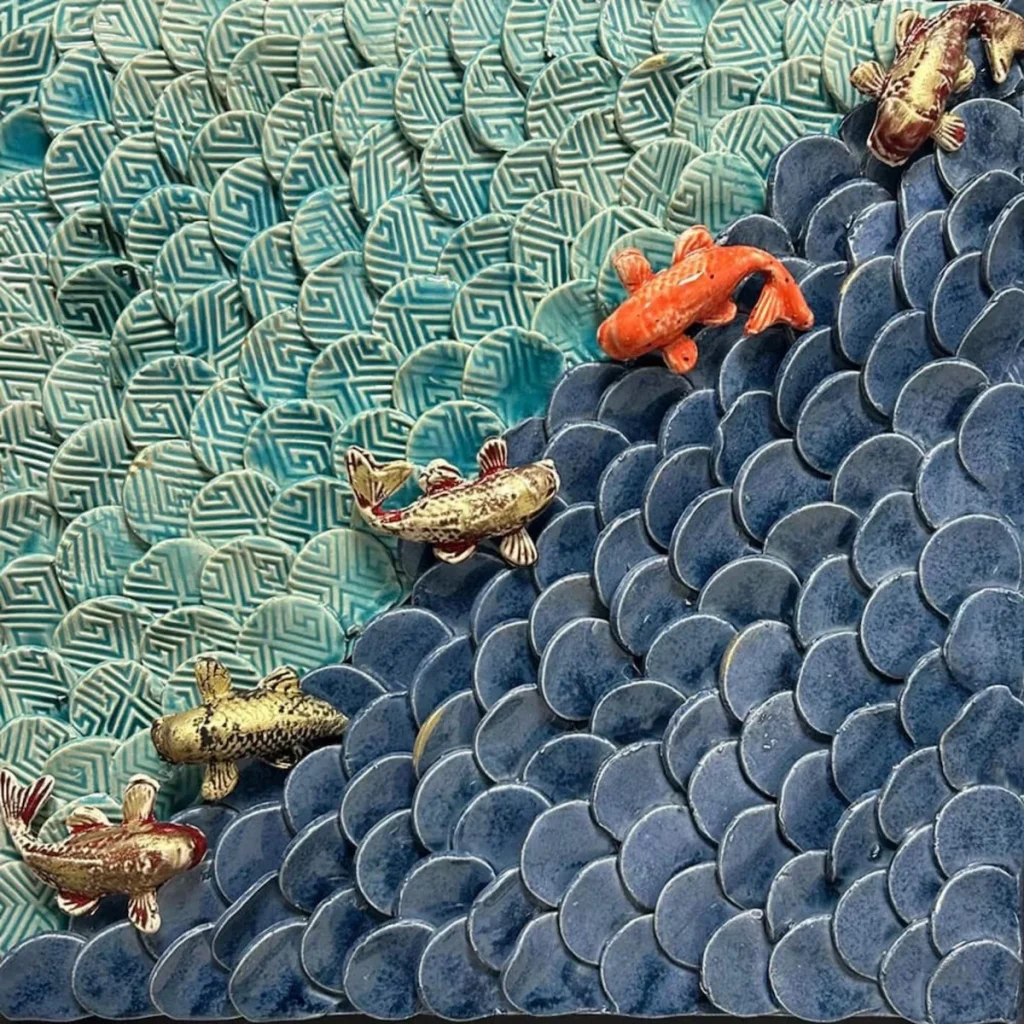 Riecha Kapoor, Tides of Change - a close up on an artwork. Small ceramic fish are transposed onto blue ceramic petals. 